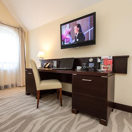 格但斯克，雷迪森布鲁酒店 外观 照片 The photo depicts a corner of a room featuring a stylish desk with a chair and a television mounted on the wall above. The desk has various items on it, possibly including a telephone, clock, and some decorative elements or stationery. There is a lam