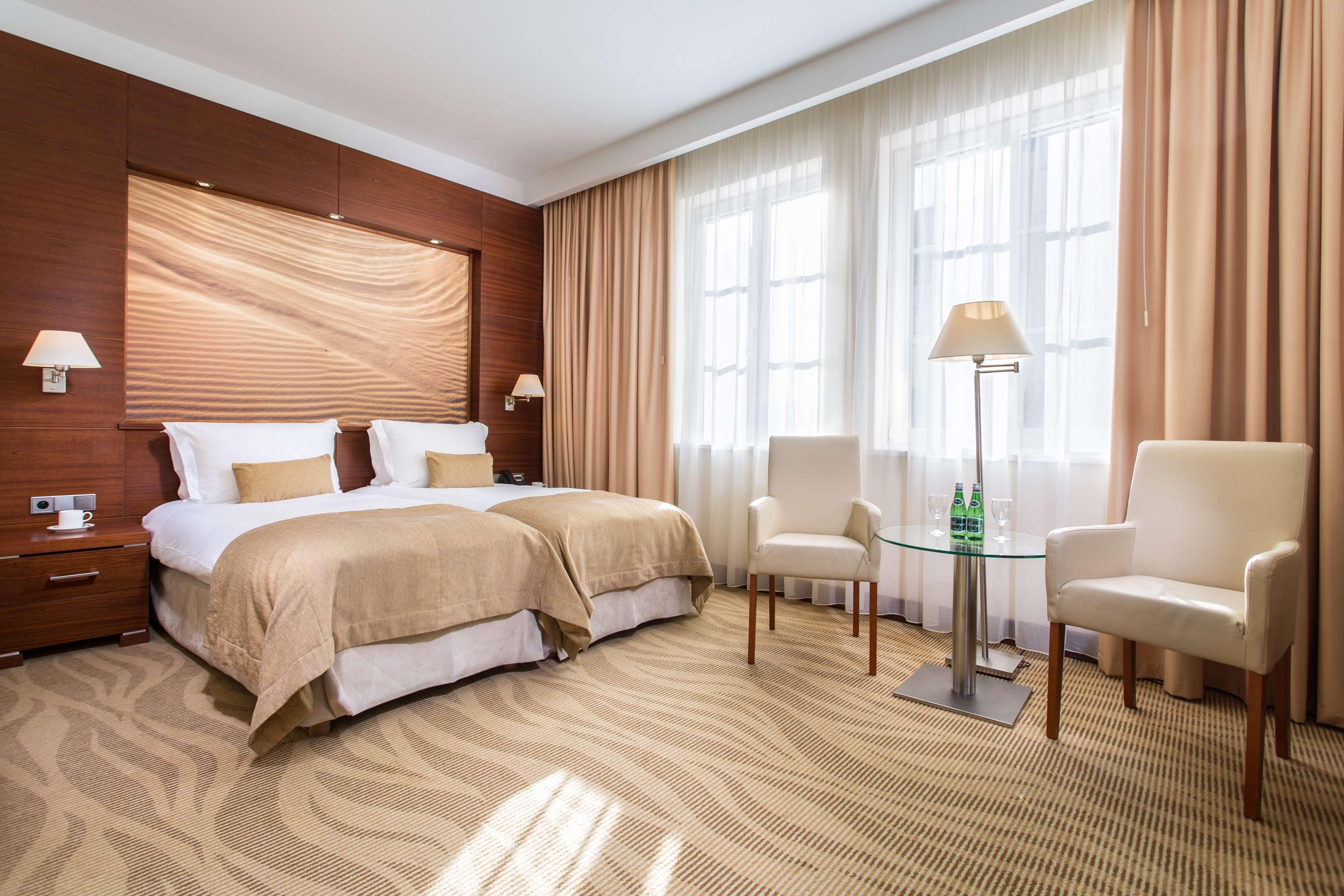 格但斯克，雷迪森布鲁酒店 外观 照片 The photo shows a well-decorated hotel room featuring two twin beds with beige linens and pillows. The walls have a warm, wooden paneling accent, and large windows are dressed with light curtains allowing natural light to fill the space. There are tw