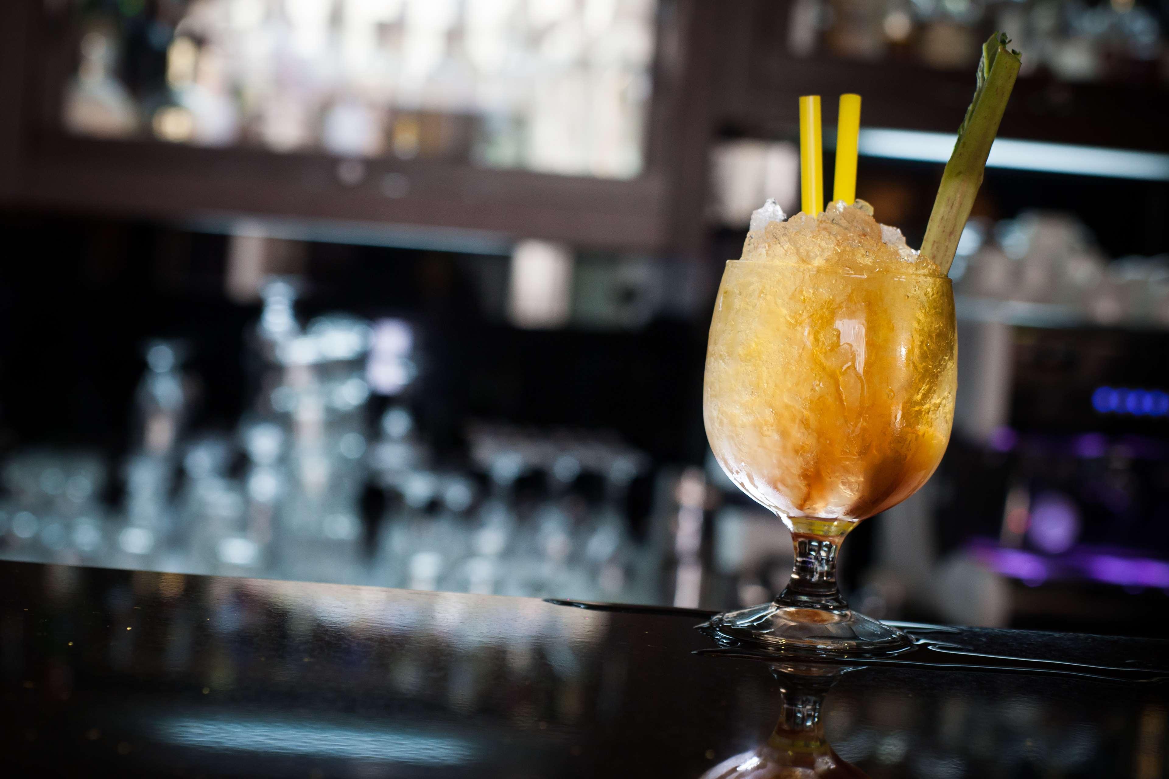 格但斯克，雷迪森布鲁酒店 外观 照片 The photo shows a cocktail served in a decorative glass. The drink appears to be slushy or frozen, with a yellow-orange hue and topped with crushed ice. It has two yellow straws and a piece of celery as garnish. The setting suggests it is in a bar or