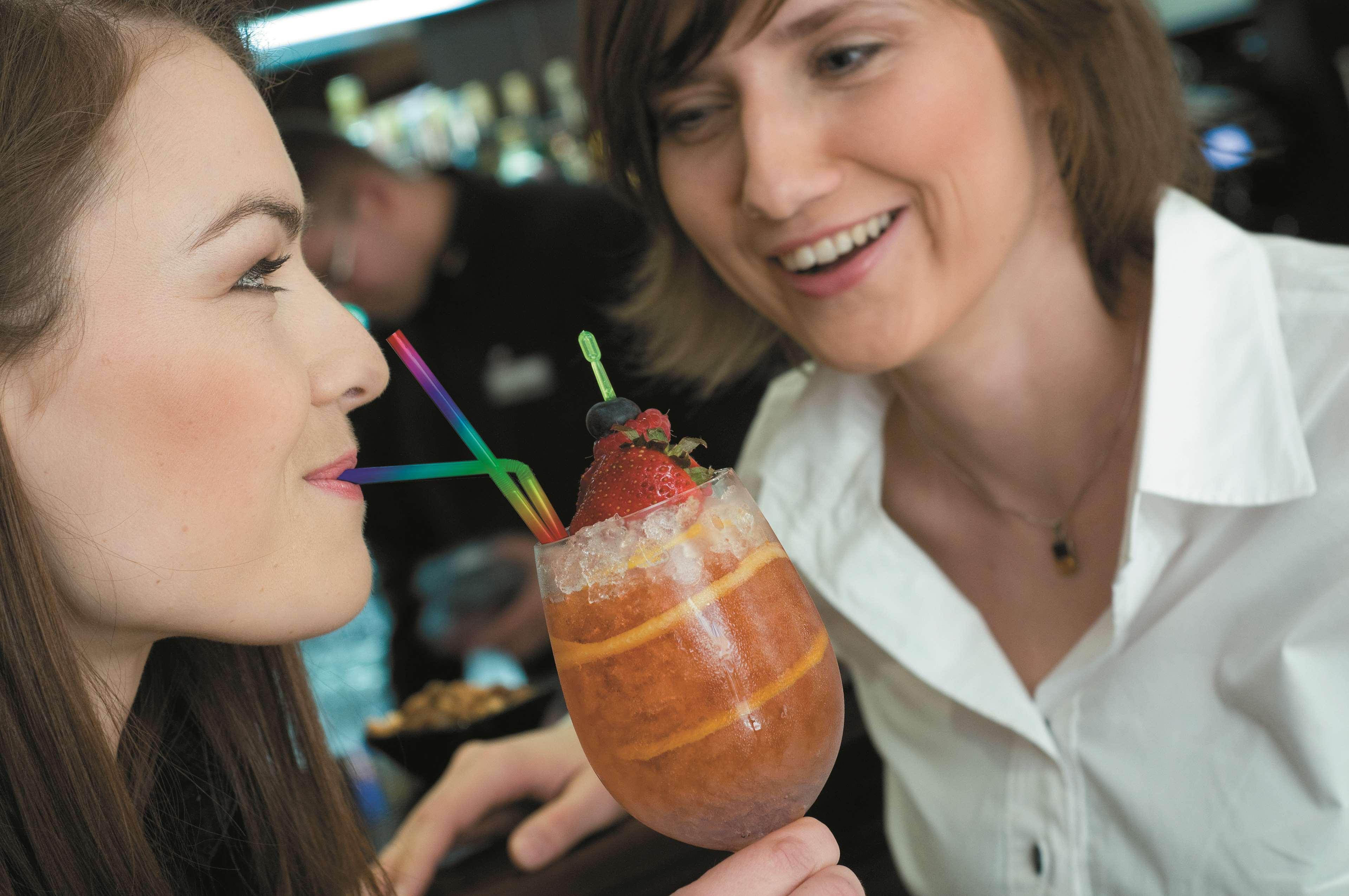 格但斯克，雷迪森布鲁酒店 外观 照片 The photo shows two women engaging with each other, smiling and enjoying a moment together. One woman is holding a colorful drink in a large glass adorned with ice, fruit, and multiple straws. The other woman looks on with a friendly expression, cont