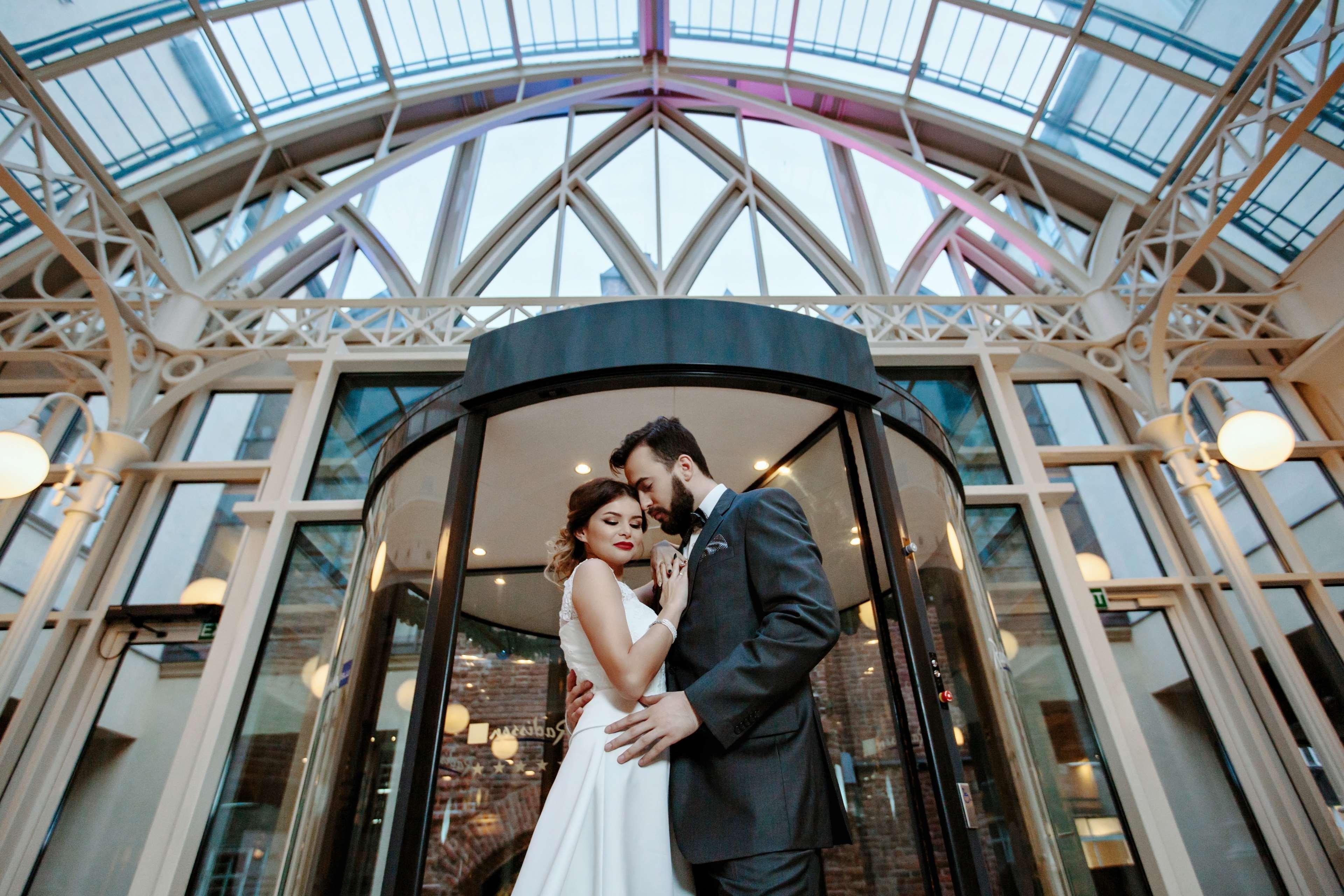 格但斯克，雷迪森布鲁酒店 外观 照片 The photo shows a romantic scene featuring a couple in formal attire, likely celebrating their wedding. They are positioned in front of a round glass door, which is partially open. The couple is standing close together, with their foreheads touching,