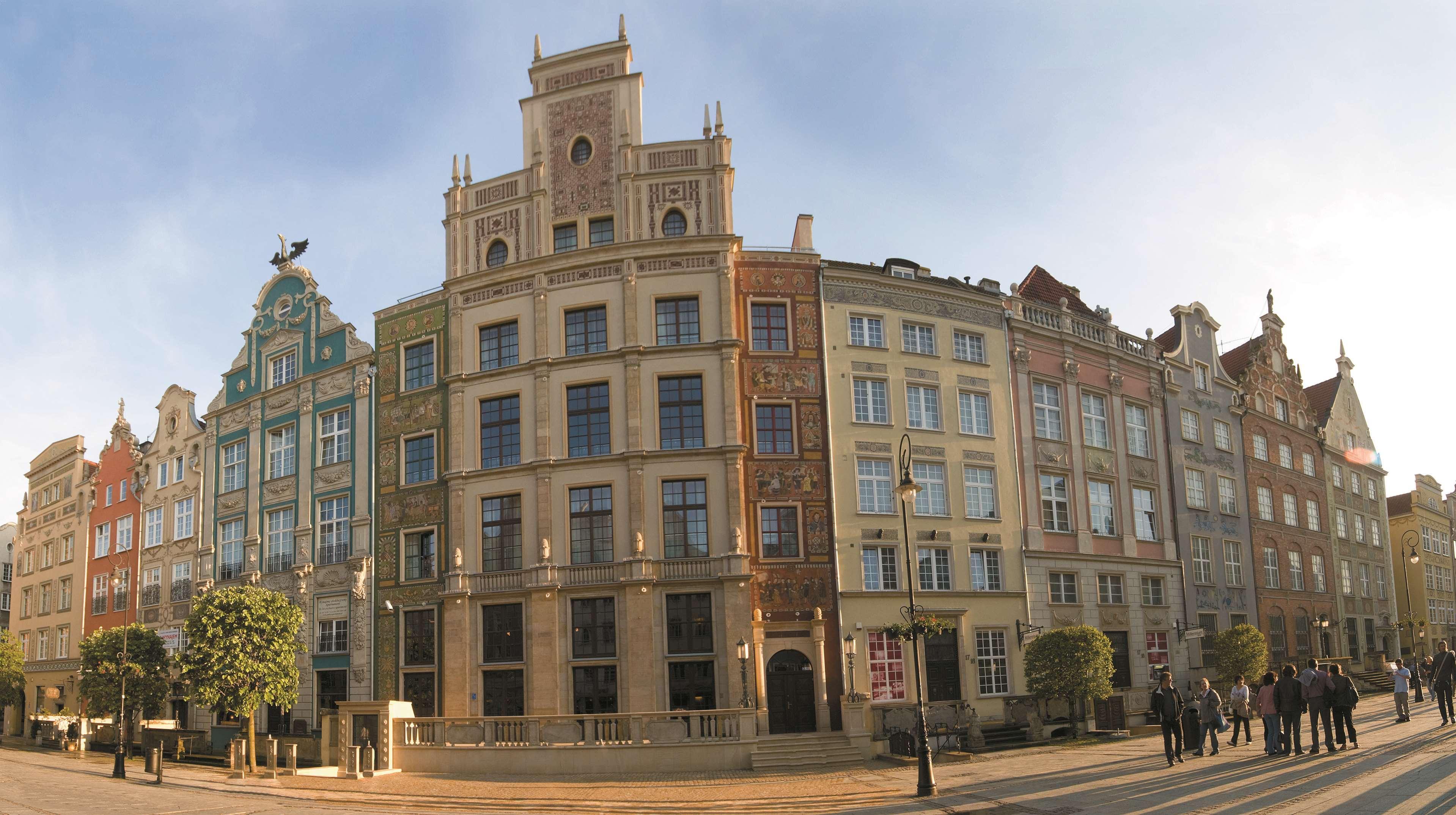 格但斯克，雷迪森布鲁酒店 外观 照片 The photo showcases a panoramic view of a row of historic buildings, likely in a European city. The architecture features a blend of styles, presenting a vibrant facade with multiple colors and decorative elements. Each building has distinct characte