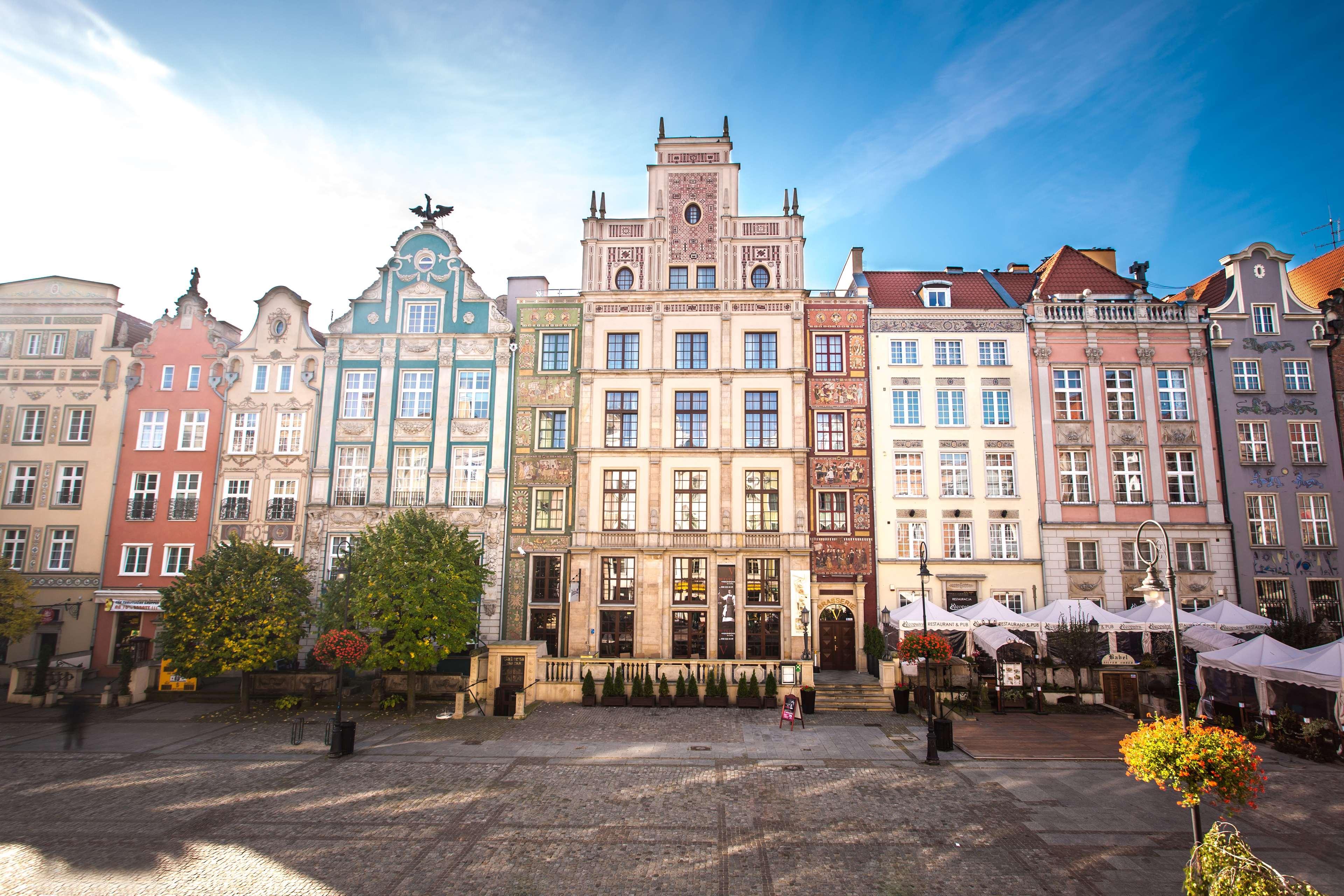 格但斯克，雷迪森布鲁酒店 外观 照片 The photo depicts a picturesque square in a historic European city, likely Gdańsk, Poland. The scene features an array of colorful, well-preserved buildings with ornate architectural details. These buildings are characterized by vibrant facades in va