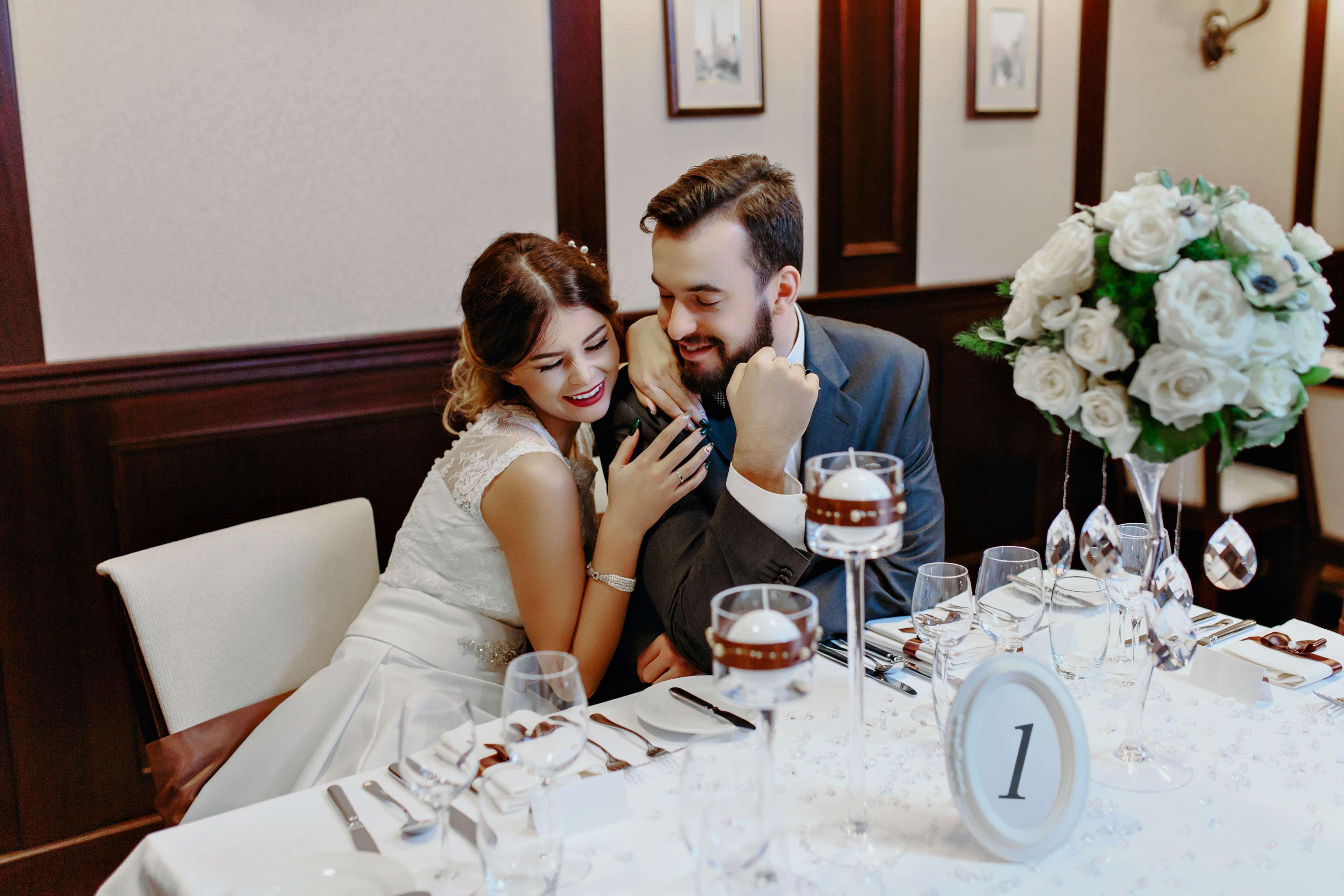 格但斯克，雷迪森布鲁酒店 外观 照片 The photo depicts a couple sitting at a beautifully arranged dining table. The woman, dressed in a white wedding gown, leans affectionately towards the man, who is wearing a gray suit. They appear to be enjoying a moment together, smiling and engagin