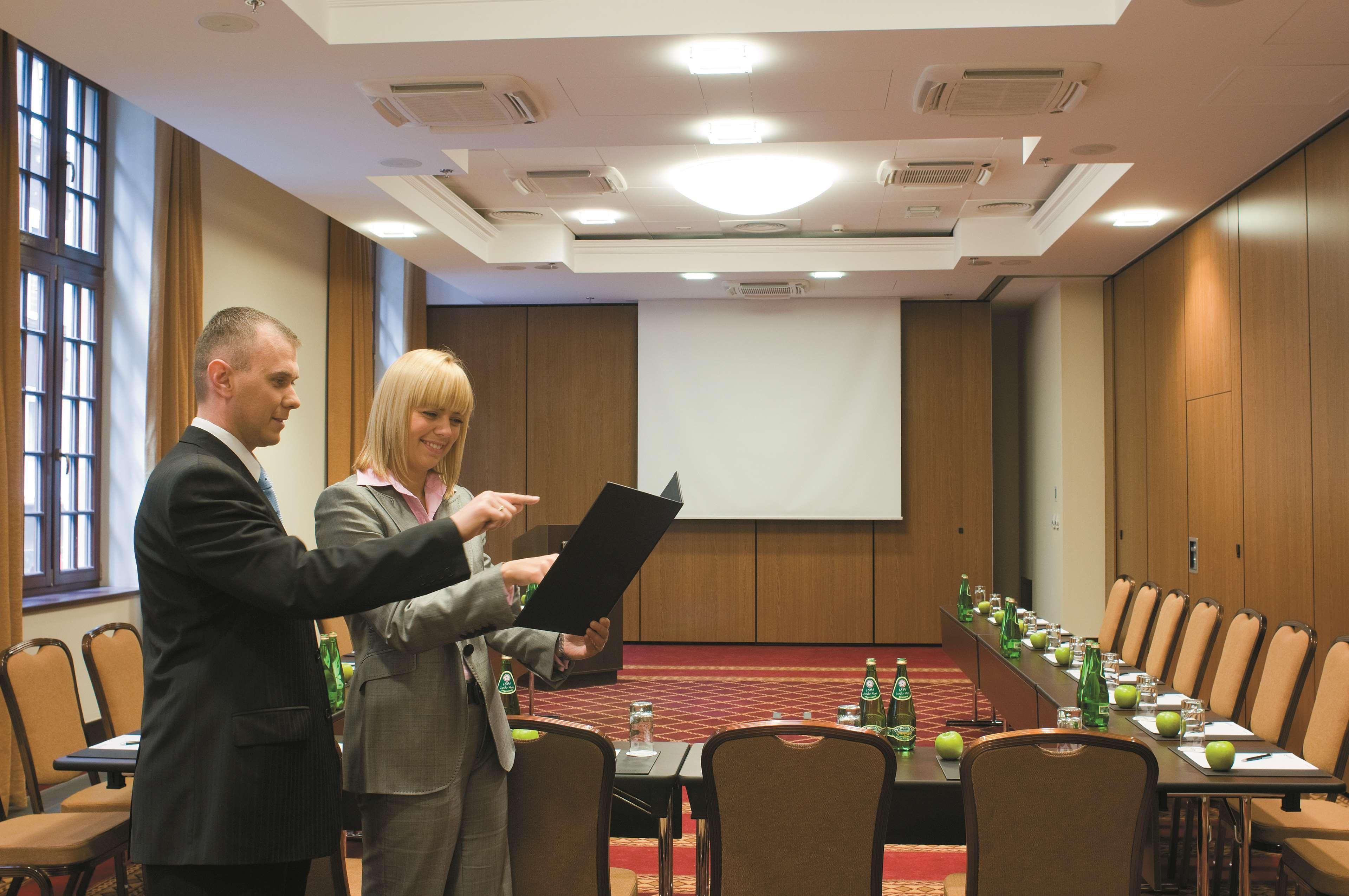 格但斯克，雷迪森布鲁酒店 设施 照片 The image shows a professional meeting room set up for a conference or presentation. There are two people in formal attire engaged in discussion; one is holding a document or folder while the other is pointing at it. The room features a large screen 