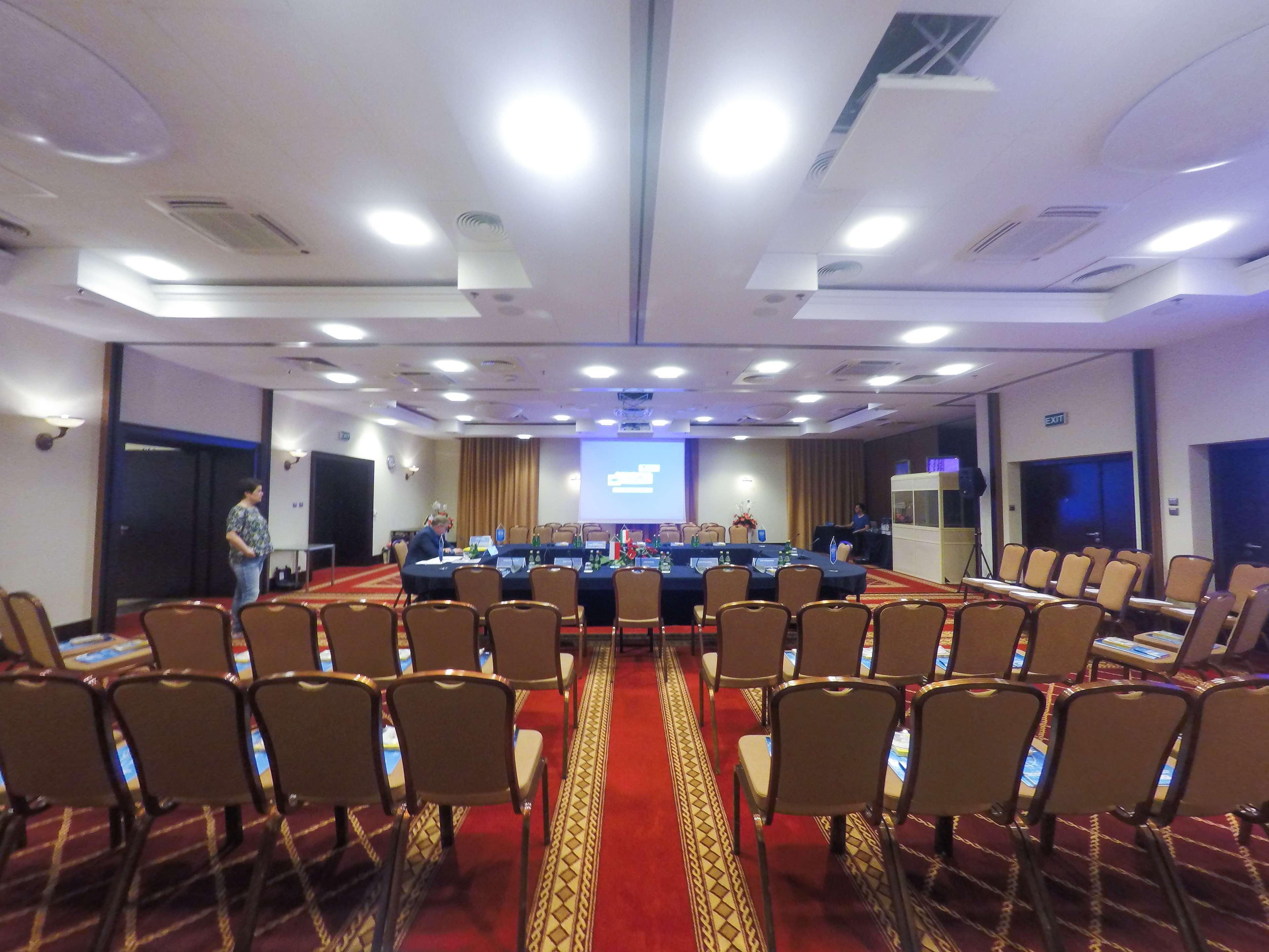 格但斯克，雷迪森布鲁酒店 外观 照片 The photo shows a conference room set up for a meeting or presentation. There are several rows of beige chairs arranged in front of a long table, which is also set up for participants. A large screen or projector is positioned at the front of the roo