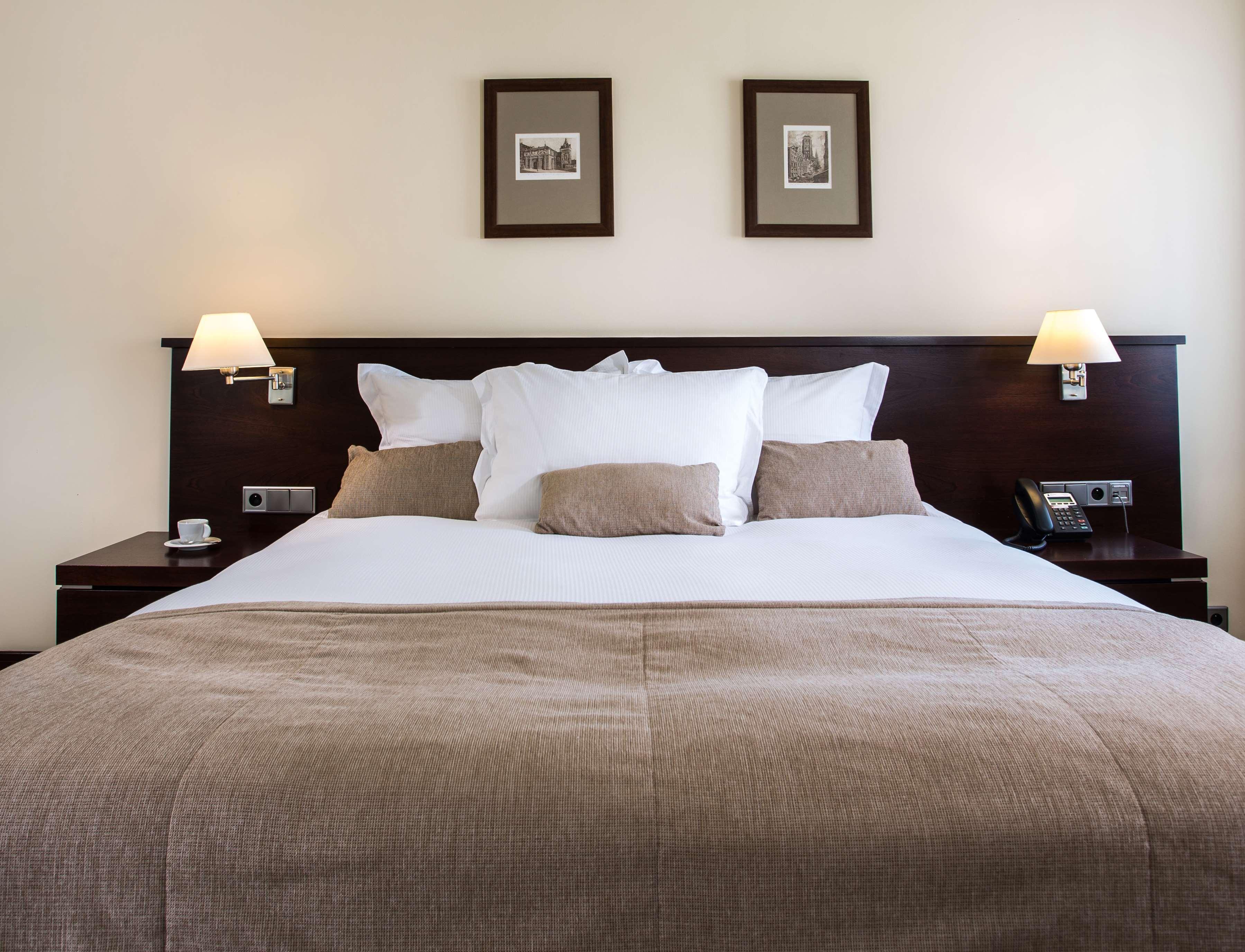 格但斯克，雷迪森布鲁酒店 外观 照片 The photo shows a well-decorated hotel room, focusing on a large bed with a dark wood headboard. The bed is adorned with several white pillows and a couple of beige cushions. There are two lamps on either side of the bed, providing soft lighting. Abo