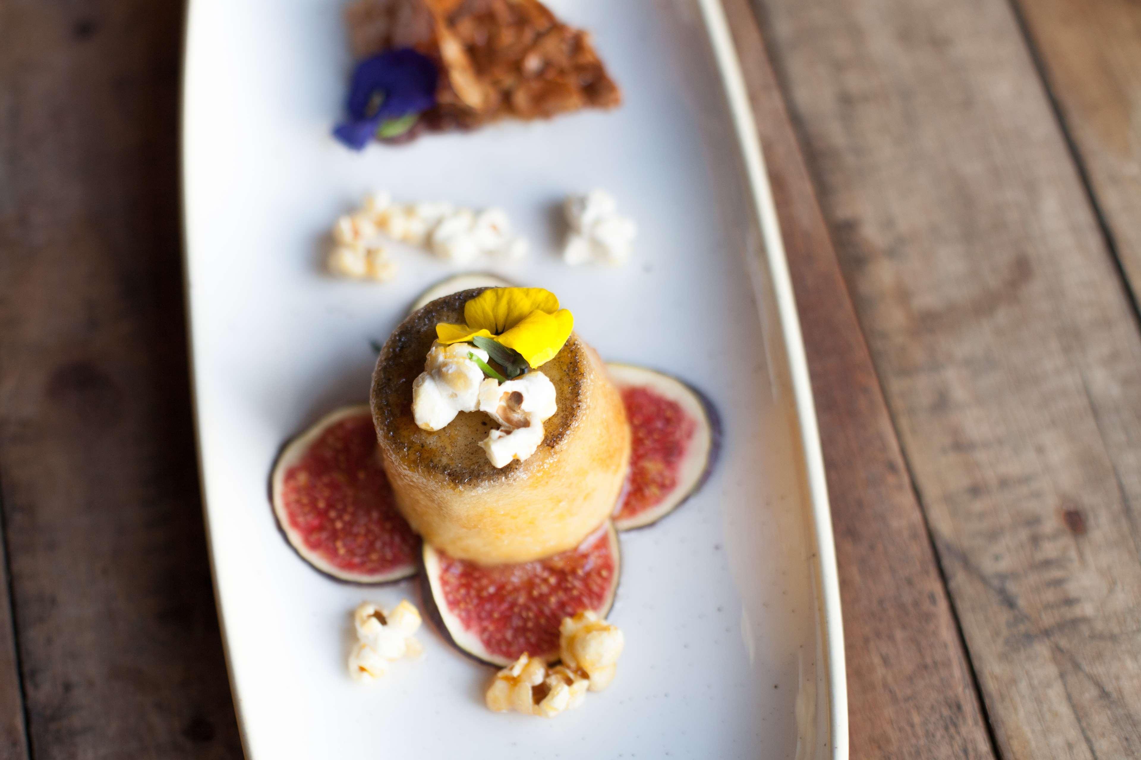 格但斯克，雷迪森布鲁酒店 外观 照片 The photo features an elegantly presented dessert on a white plate. In the center, there is a small dome-shaped cake topped with a yellow flower and popcorn. Surrounding it are slices of fig and scattered popcorn. To the side, there is a piece of a c