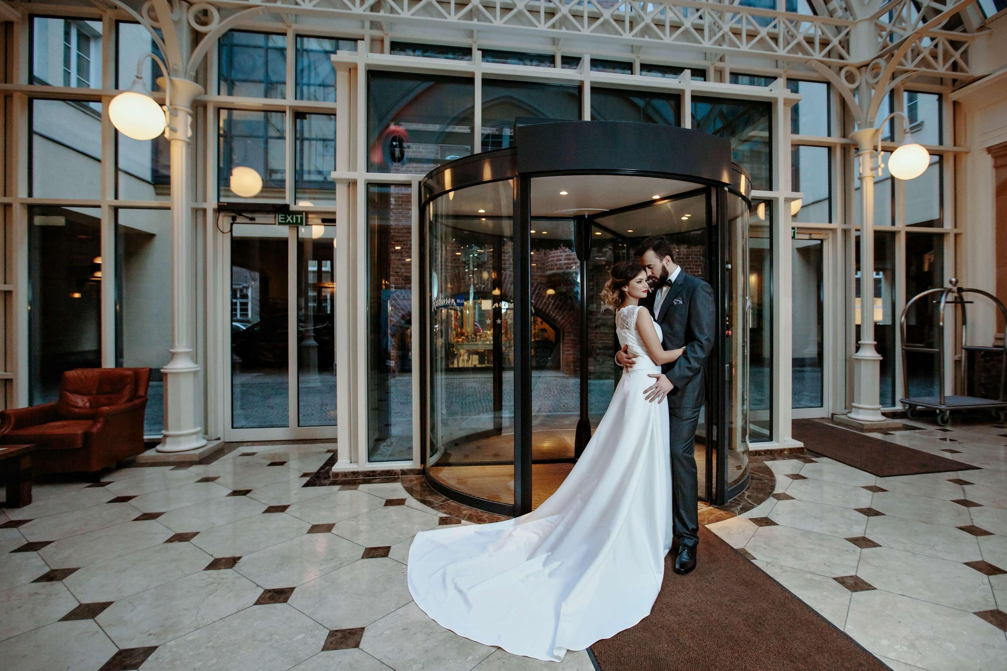 格但斯克，雷迪森布鲁酒店 外观 照片 The photo shows a couple in formal attire standing outside a building, likely a hotel or venue. They appear to be newlyweds, with the woman in a beautiful white wedding gown and the man in a suit. They embrace each other tenderly in front of a glass 