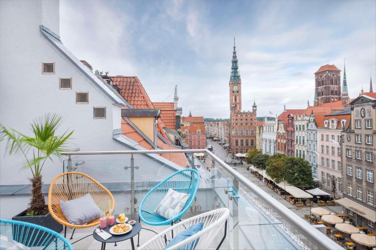 格但斯克，雷迪森布鲁酒店 外观 照片 The photo shows a stylish balcony overlooking a scenic urban landscape. There are two colorful chairs in blue and white, positioned around a small table. On the table, there are desserts and drinks, suggesting a cozy spot for relaxation. In the backg