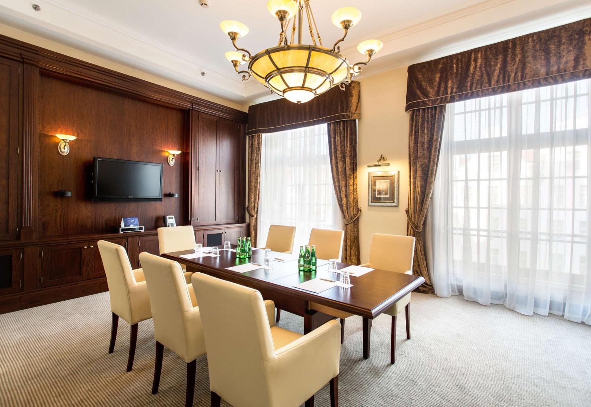 格但斯克，雷迪森布鲁酒店 外观 照片 The photo shows a well-furnished conference room. It features a large wooden table surrounded by six cream-colored chairs. On the table, there are several green glass bottles of water. The room is well-lit with a decorative chandelier hanging from th