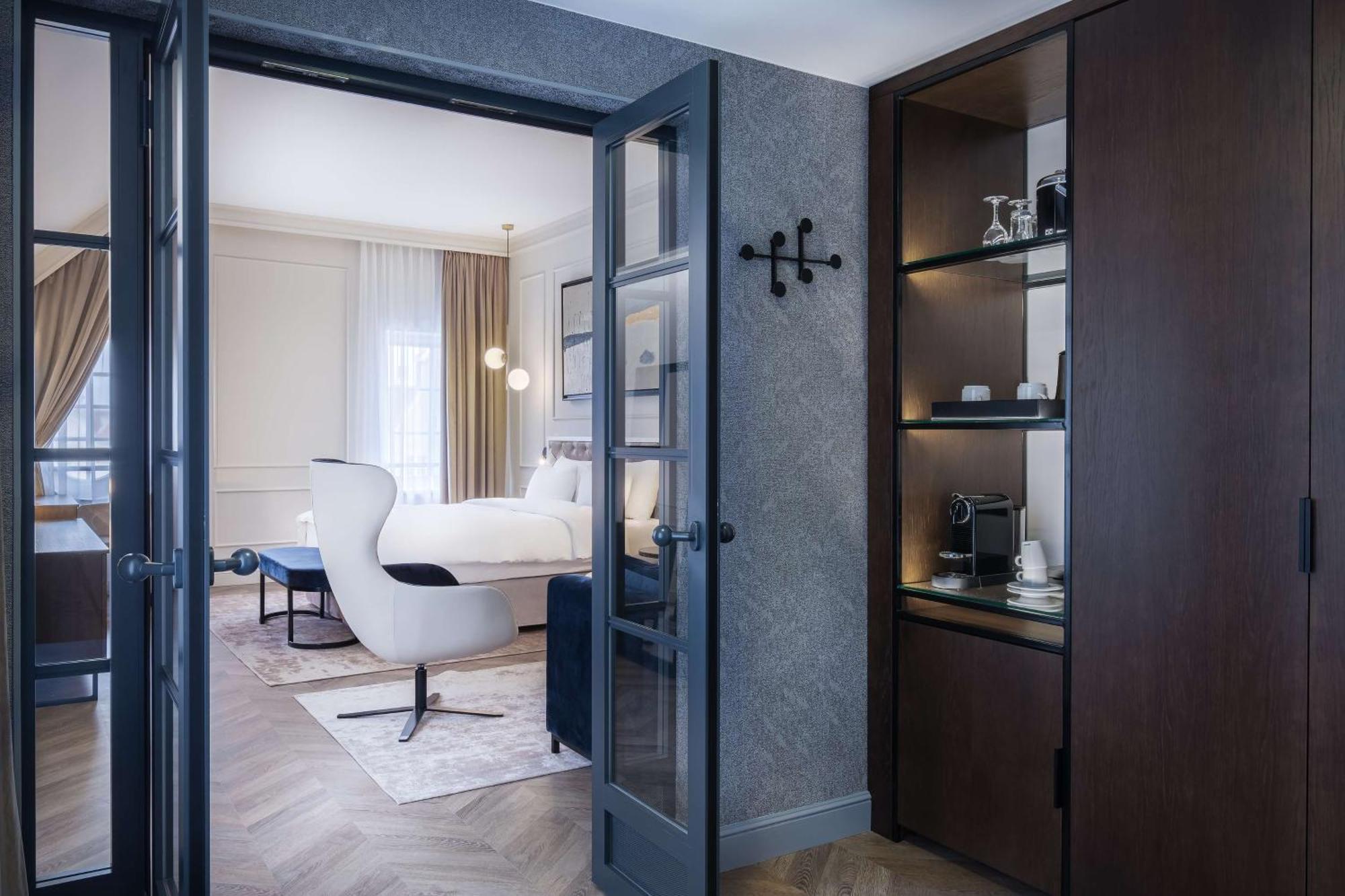 格但斯克，雷迪森布鲁酒店 外观 照片 The photo shows a luxuriously designed hotel room viewed from an entrance. In the foreground, there is a doorway with dark double doors leading into the main area. To the right, there is a wooden cabinet with shelves displaying some items, including 