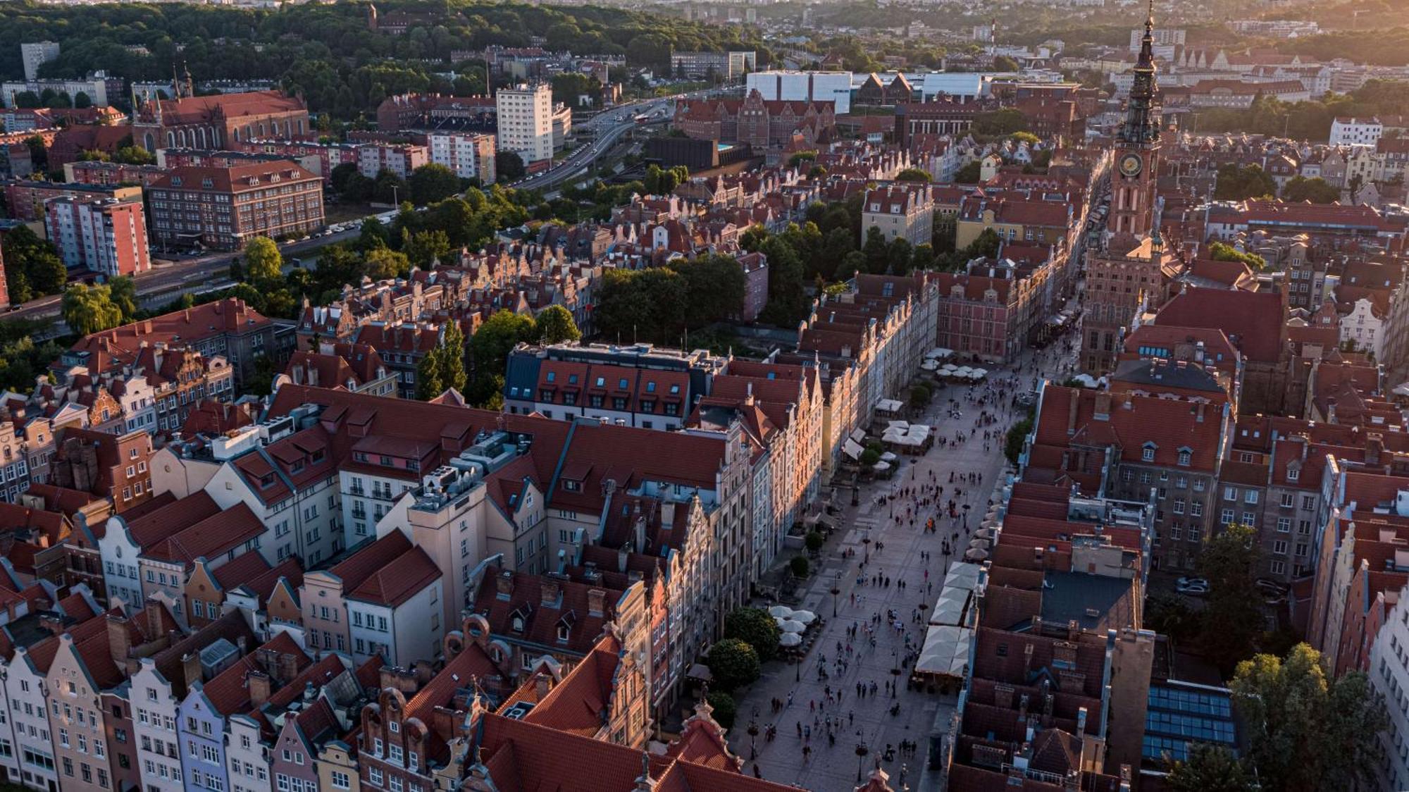 格但斯克，雷迪森布鲁酒店 外观 照片 The photo depicts a scenic aerial view of a city, likely Gdańsk in Poland. The landscape features historical buildings with distinctive architecture, characterized by colorful facades and prominent rooftop designs. A bustling street runs through the 
